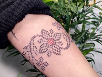 Un avant-bras avec un tatouage noir et rouge représentant une  motif floral, en point de croix